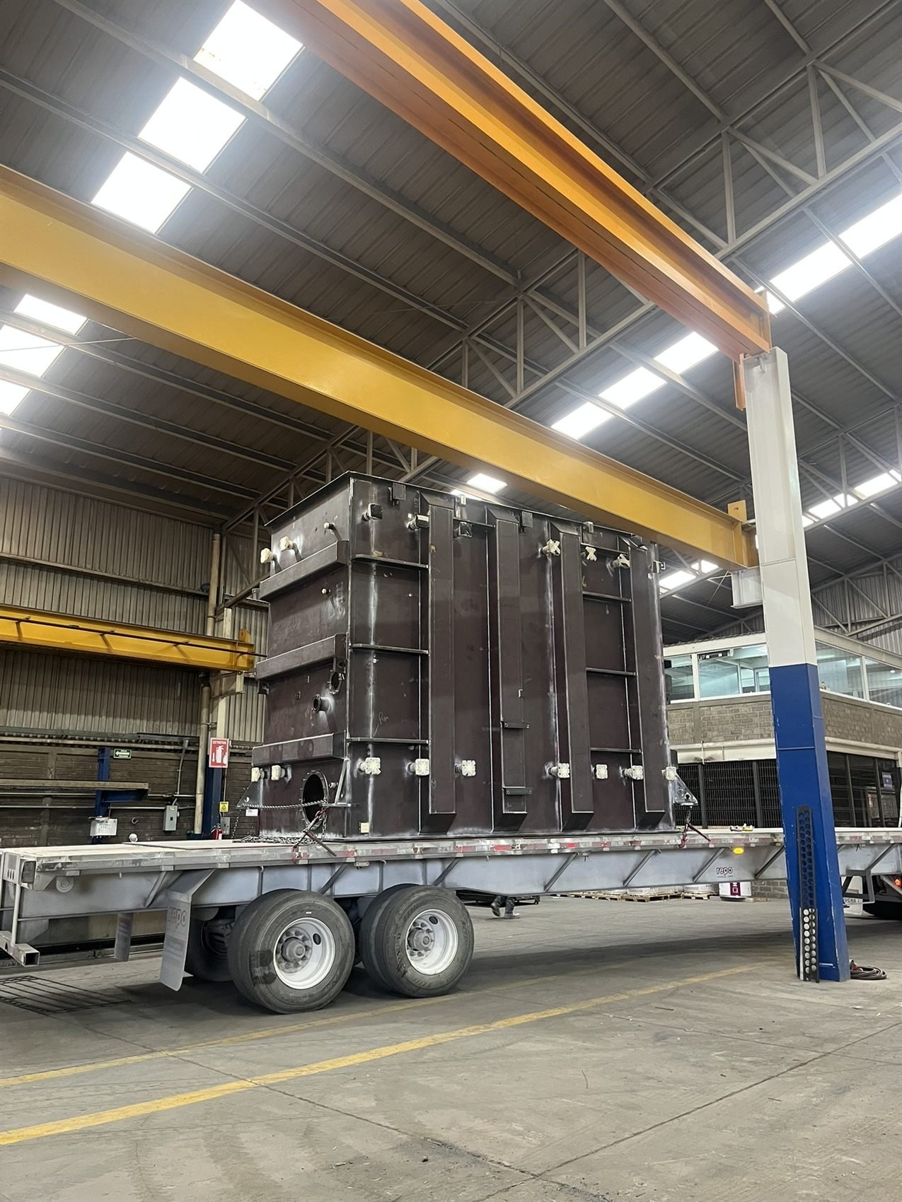 Transformer tank on a flatbed trailer under an overhead crane